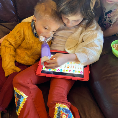 Young siblings, boy and girl, sit in a chair looking at an ipad. 