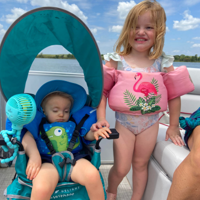 Young boy sleeps in a chair next to his sister, both in swimsuits, on a boat, with water in the background. 