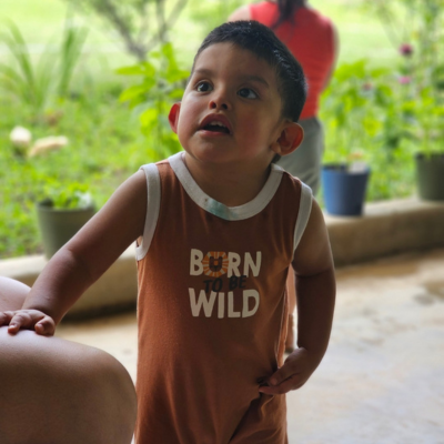 Toddler boy with dark brown hair looks up, wearing a Born Wild t-shirt. 