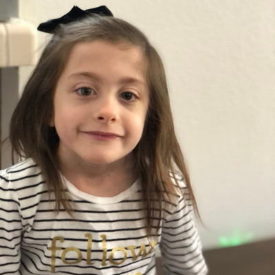 Young girl with brown hair wearing a striped shirt and a black bow in her hair. 
