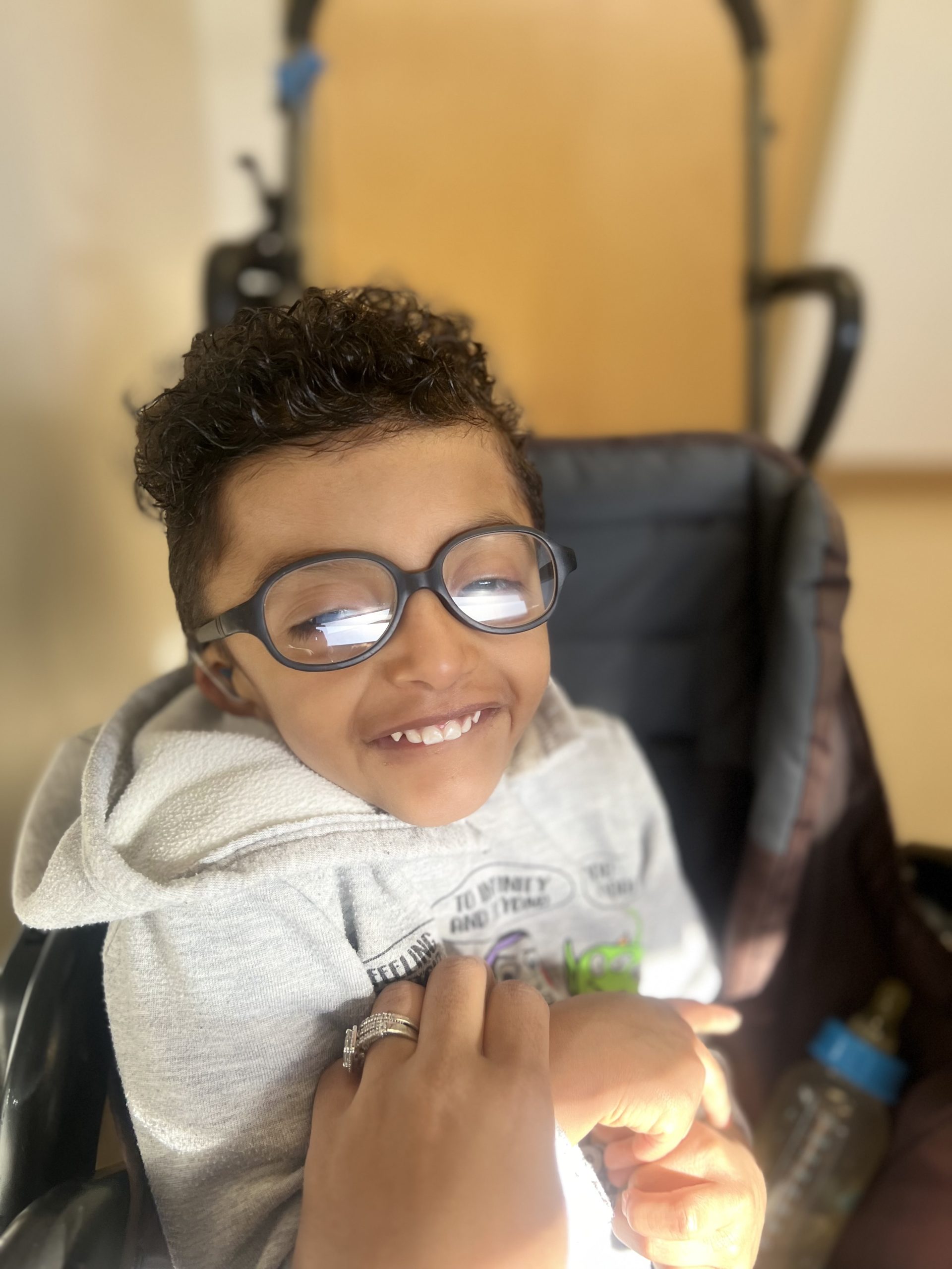 Young boy with curly hair and glasses smiles.