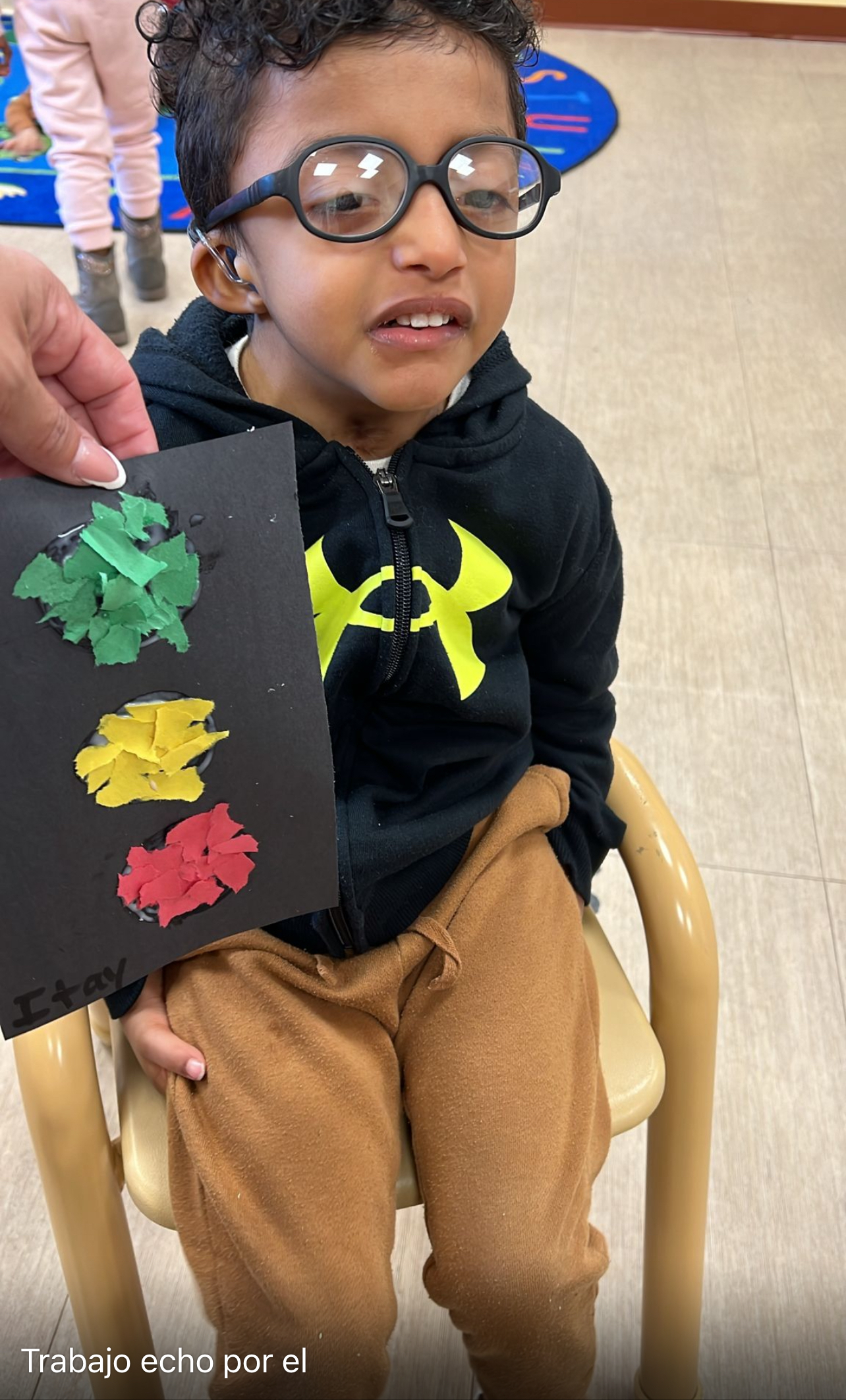 Young boy with glasses proudly holds up a craft he made.