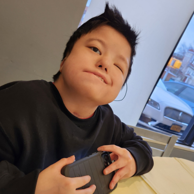Young boy in black sweatshirt, with black hair, poses at table with cell phone in hand. 