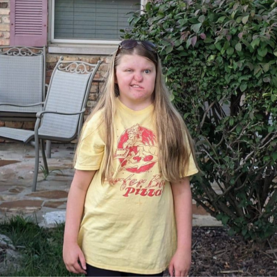 Girl in a yellow shirt with long blonde hair poses outside.