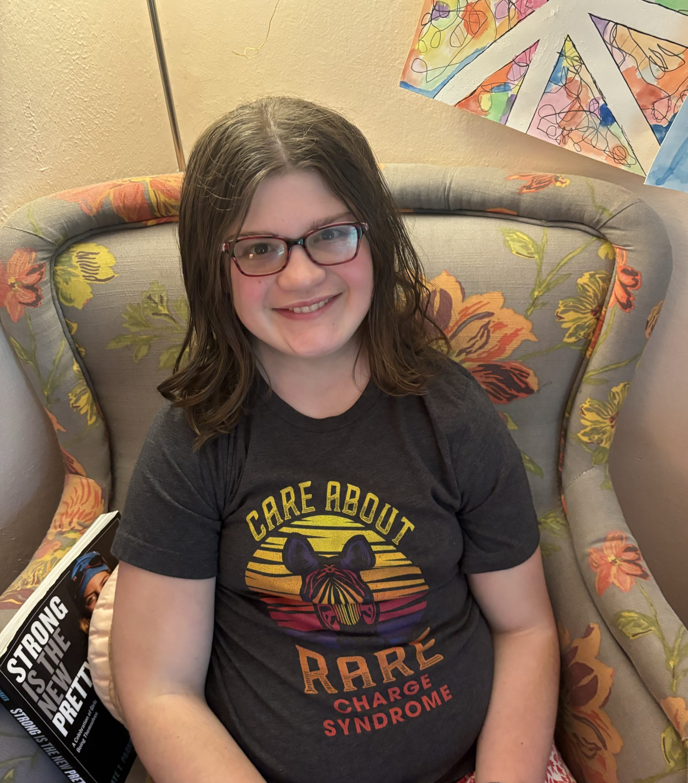 Photo of teenage girl in glasses wearing a shirt with a zebra on it that says Care About Rare - CHARGE syndrome. 