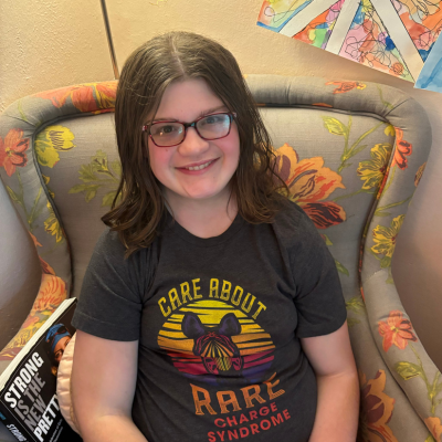 Photo of teenage girl in glasses wearing a shirt with a zebra on it that says Care About Rare - CHARGE syndrome. 