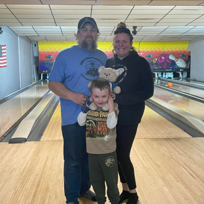 Father and Mother pose with young son in front of bowling lane. 