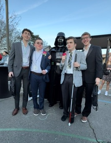 Four young men in suits pose with Darth Vader.