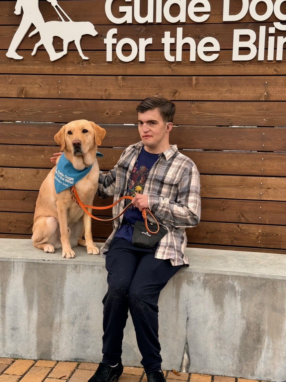Young man sits with his assistance dog, a golden retriever wearing a bandana