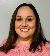 Woman in a pink top with dark brown hair smiles at the camera.