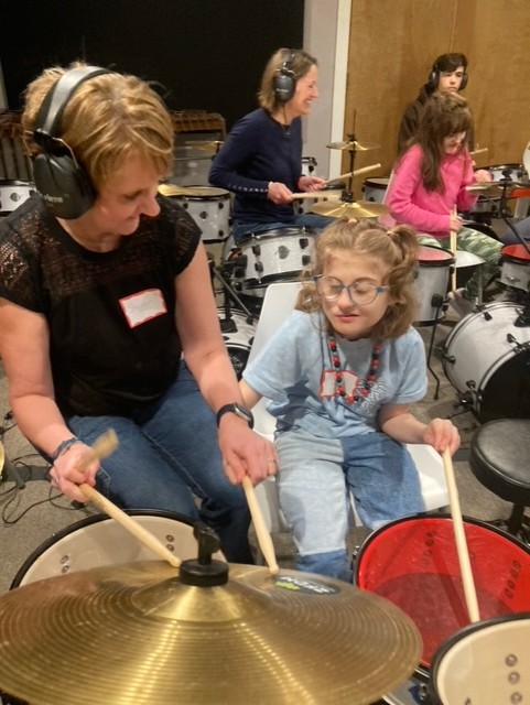 mother and daughter, with CHARGE syndrome, play a drum set.