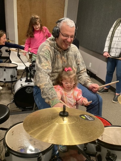 Father and young daughter, with CHARGE syndrome, play a drum set. 