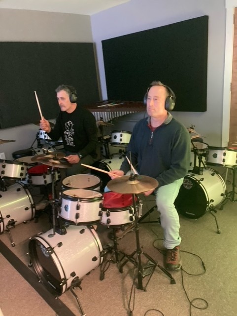 Father and son, with CHARGE syndrome, play the drum set. 