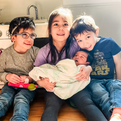 Three small children, one of whom has CHARGE syndrome, holding a newborn baby.