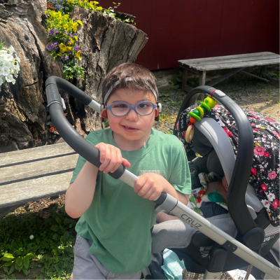 Young boy with CHARGE syndrome, wearing glasses poses with a stroller.