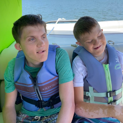 2 boys with CHARGE sit on a boat with life jackets on