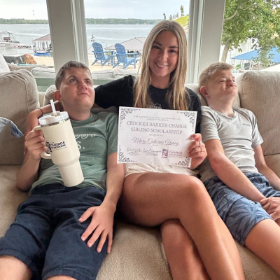 Teen girl sits on a couch presenting a certificate between her two brothers with CHARGE syndrome