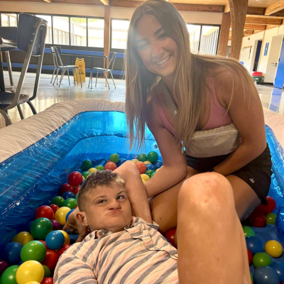Teen girl sits in a ball pit with her brother, who has CHARGE syndrome