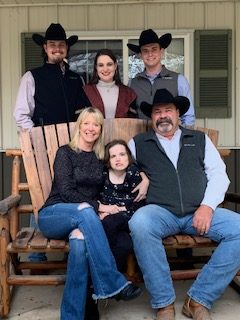 Family with 3 children poses on a front porch wearing cowboy hats