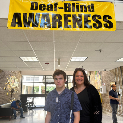 Young man and his mother pose in front of a banner that reads Deaf-Blind Awareness