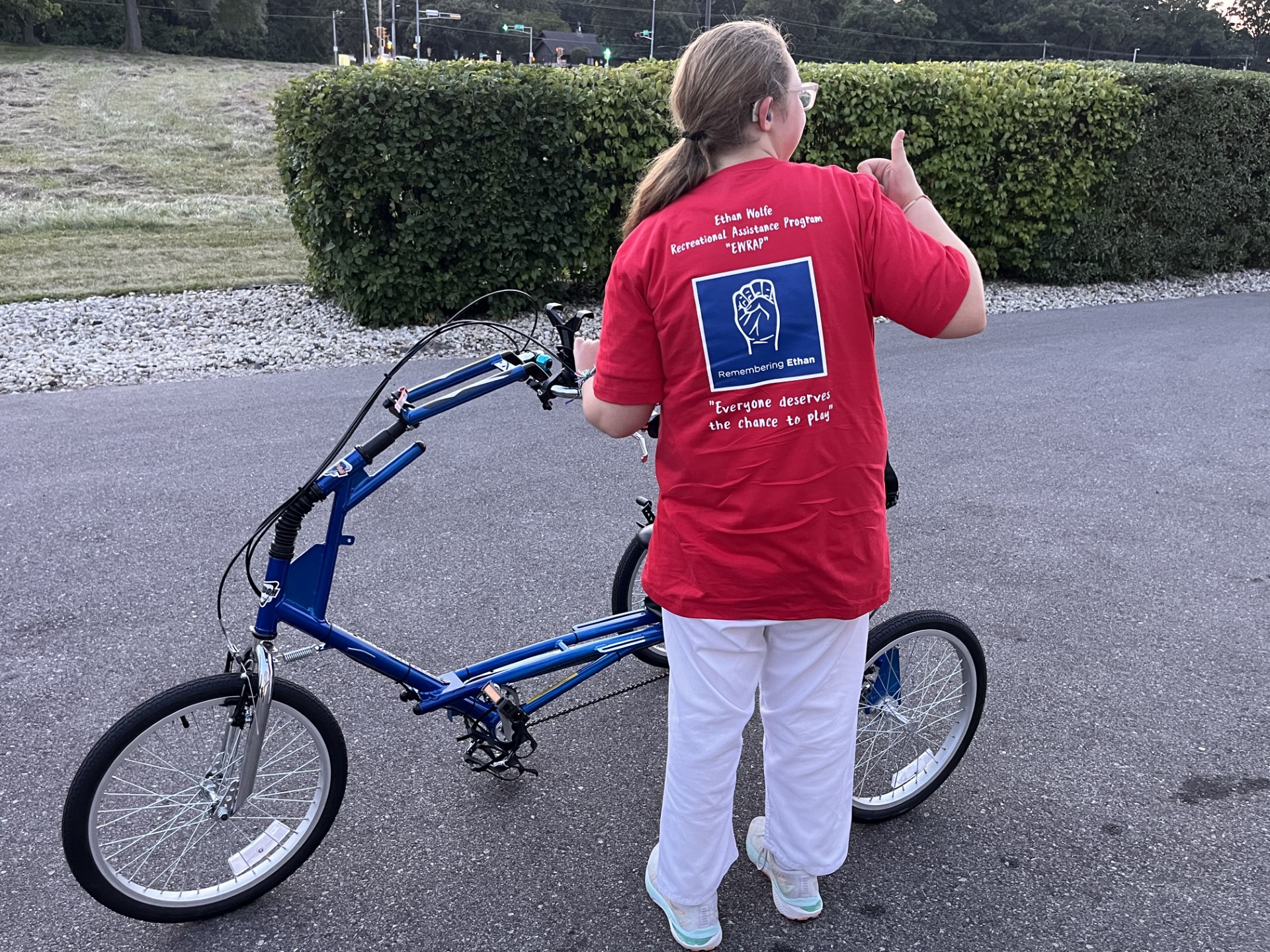 View from the back of a teenage girl and her bike. Back of her shirt has the EWRAP logo and she is giving a thumbs up. 