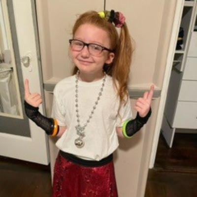 A young girl dressed in 90s costume poses and smiles. 