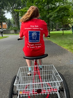 Teenage girl rides an adaptive 3-wheeled bike. Shows the back of her shirt with the EWRAP logo.