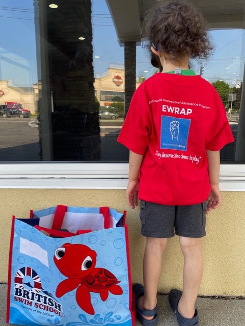Young boy poses outside the pool building wearing a shirt with the EWRAP logo. 