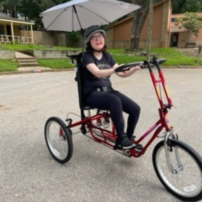 Girl with glasses rides an adaptive bike with an umbrella. 
