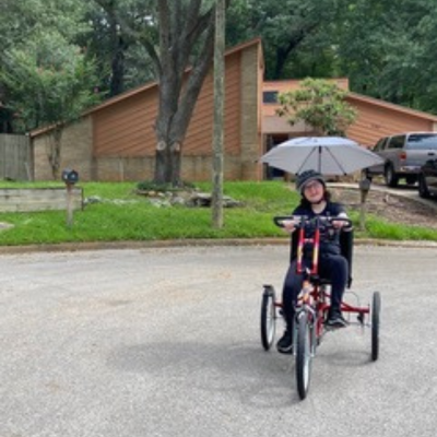 Girl with glasses rides an adaptive bike with an umbrella. 