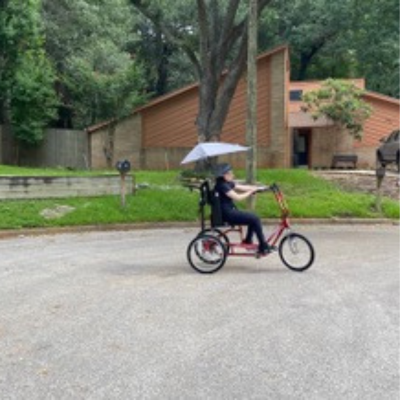 Girl with glasses rides an adaptive bike with an umbrella. 