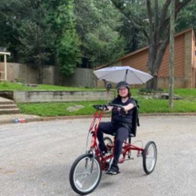 Girl with glasses rides an adaptive bike with an umbrella. 