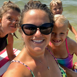 Mom poses with two daughters and one son in front of water.