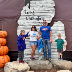 Family with two daughters and one son pose together in front of a wall design shaped like Michigan