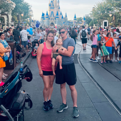mother, father, and young daughter pose in front of the castle in Disney World