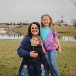Mom and two kids pose in a field with water behind them