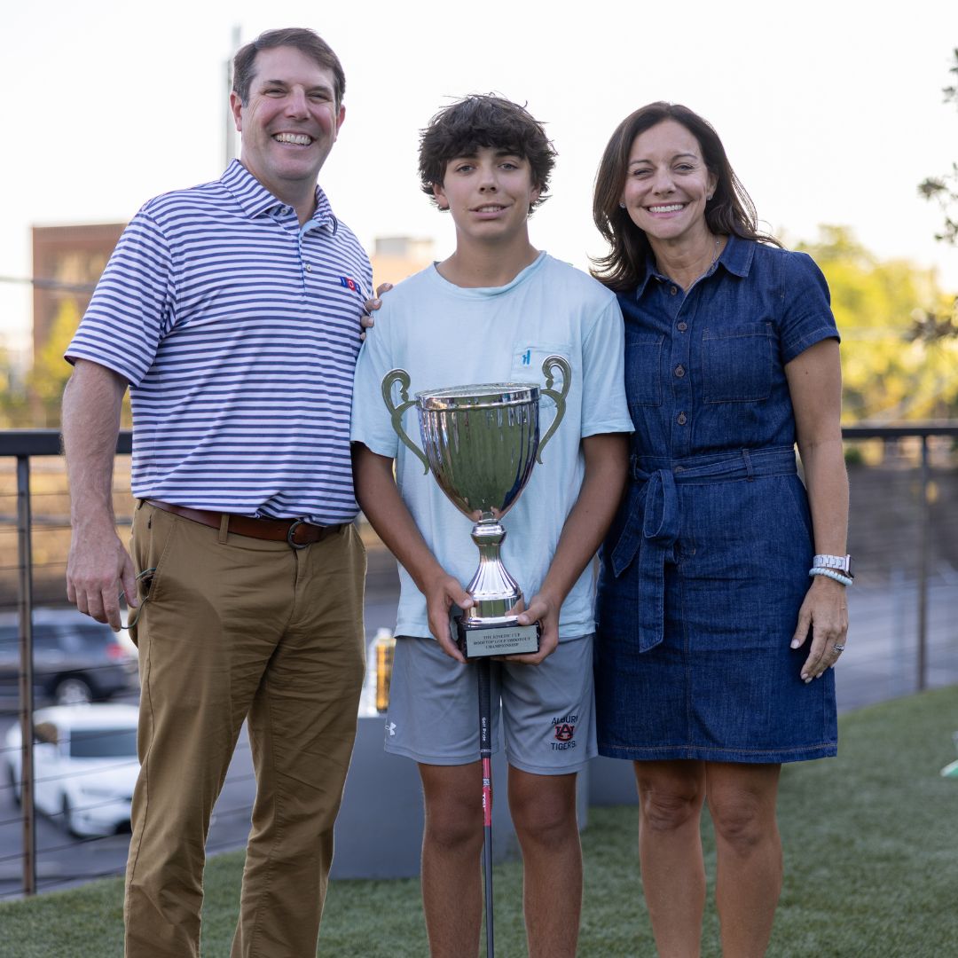 Young man poses with his parents, holding a large trophy. 