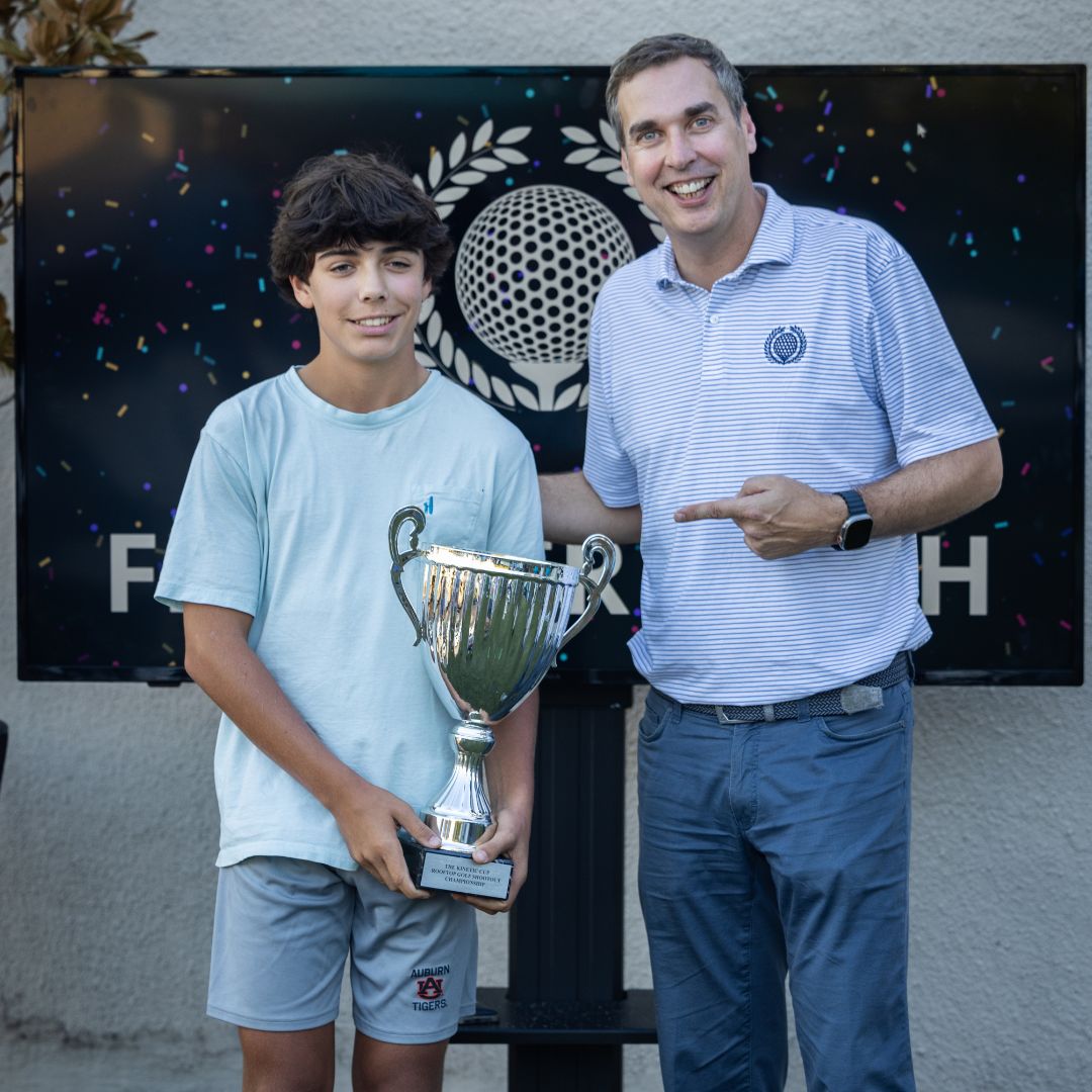 Young man poses with Jay Brandrup, holding a large trophy. 