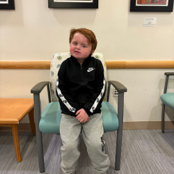 A young boy with CHARGE syndrome poses in a chair