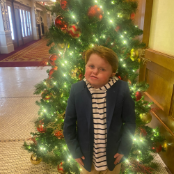 A young boy with CHARGE syndrome poses in front of a christmas tree